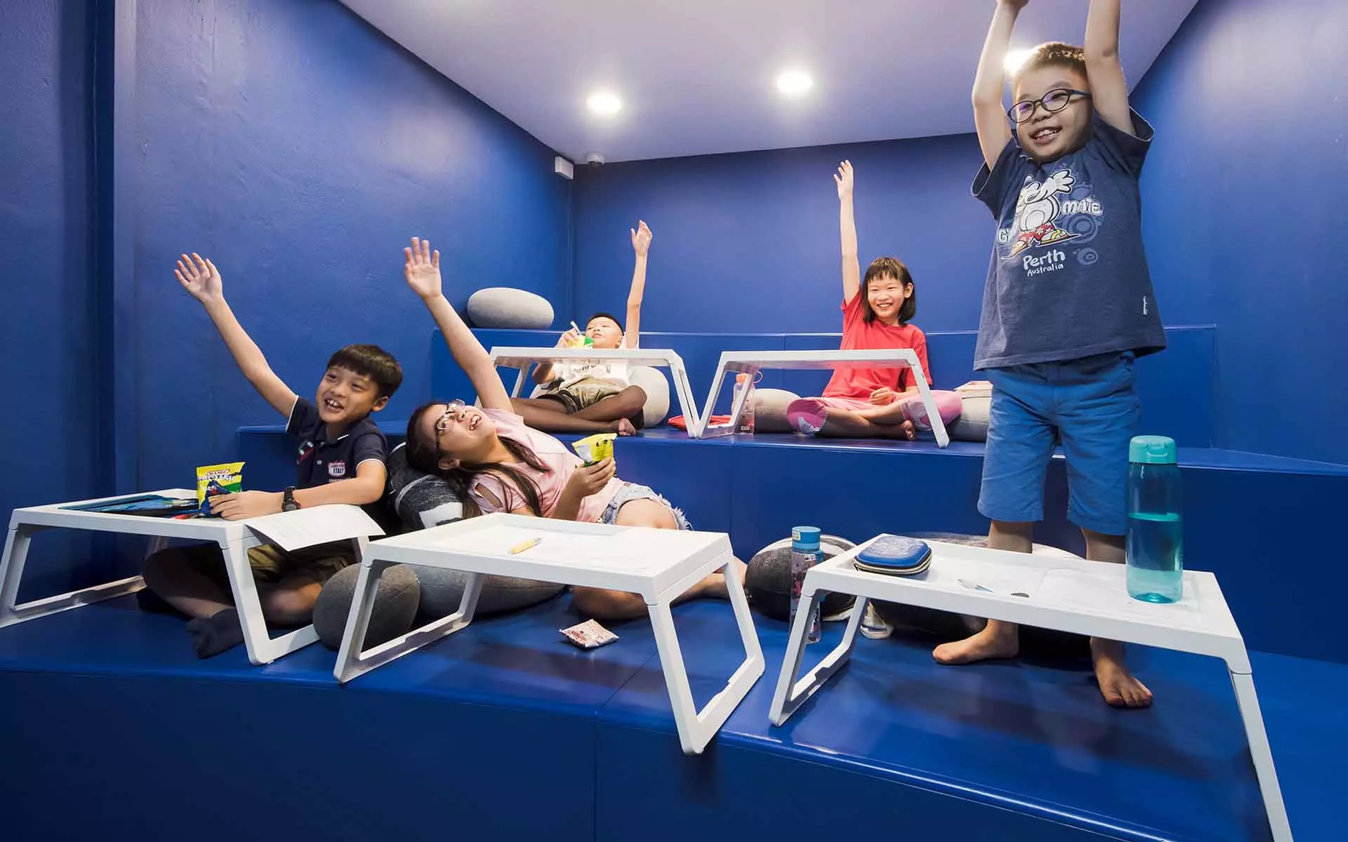 kids raising their hands and participating in a math olympiad tuition centre at a blue, non-traditional classroom setup