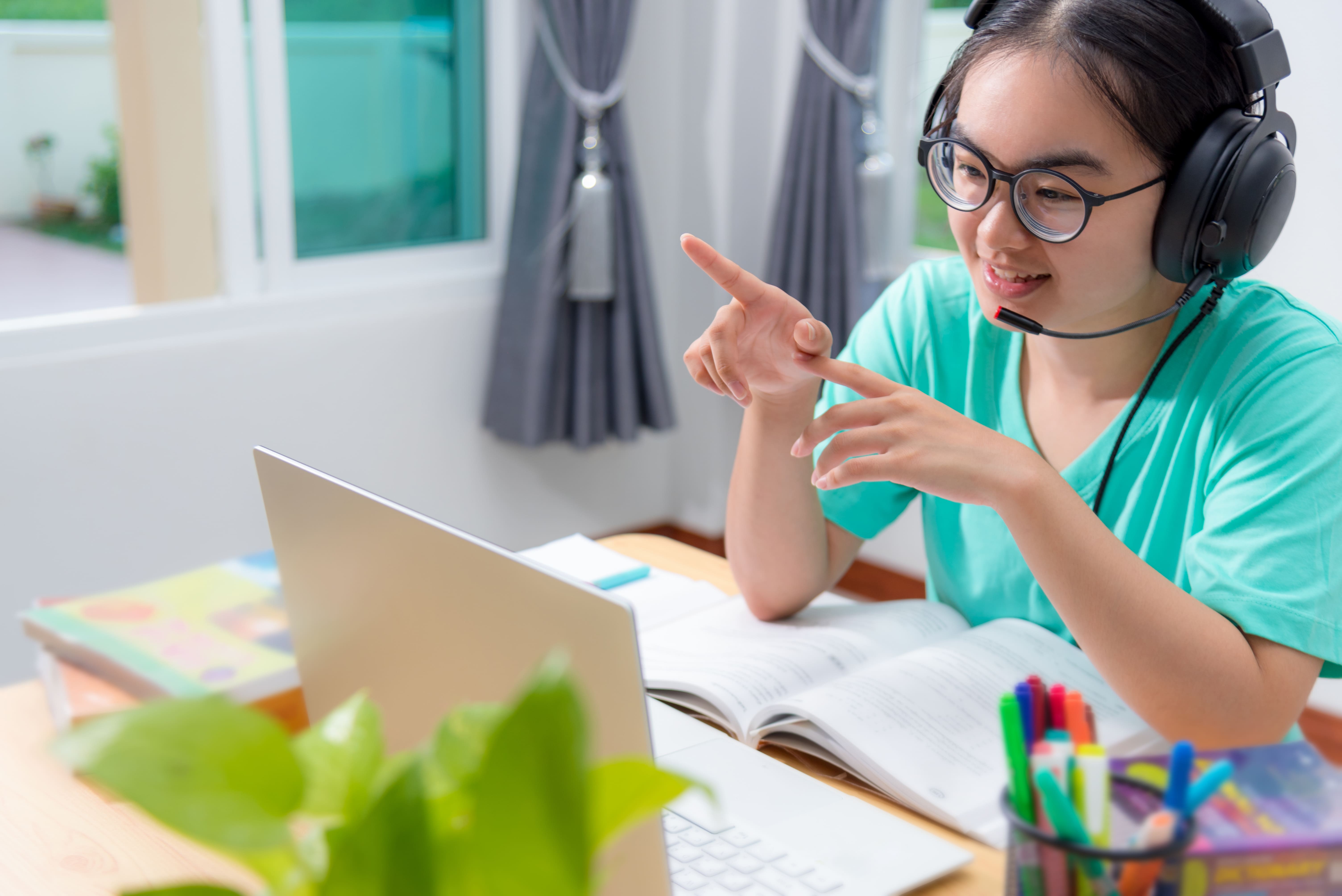  a female student wearing a headset with her laptop on the table, seemingly having an online class